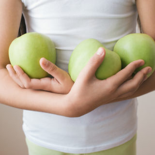 Girl in shirt holding three green apples