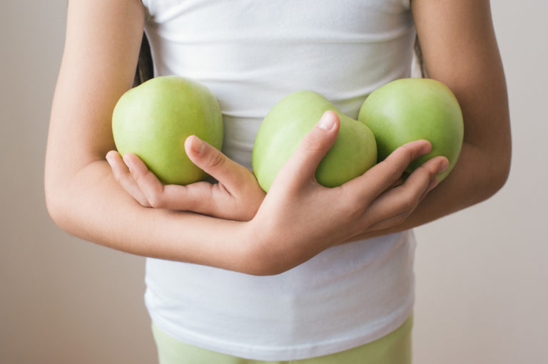 Girl in shirt holding three green apples